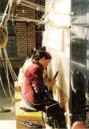 photo depicting the fine art of hand knotting a wool rug as 3 women weave in unison on a large vertical loom - China